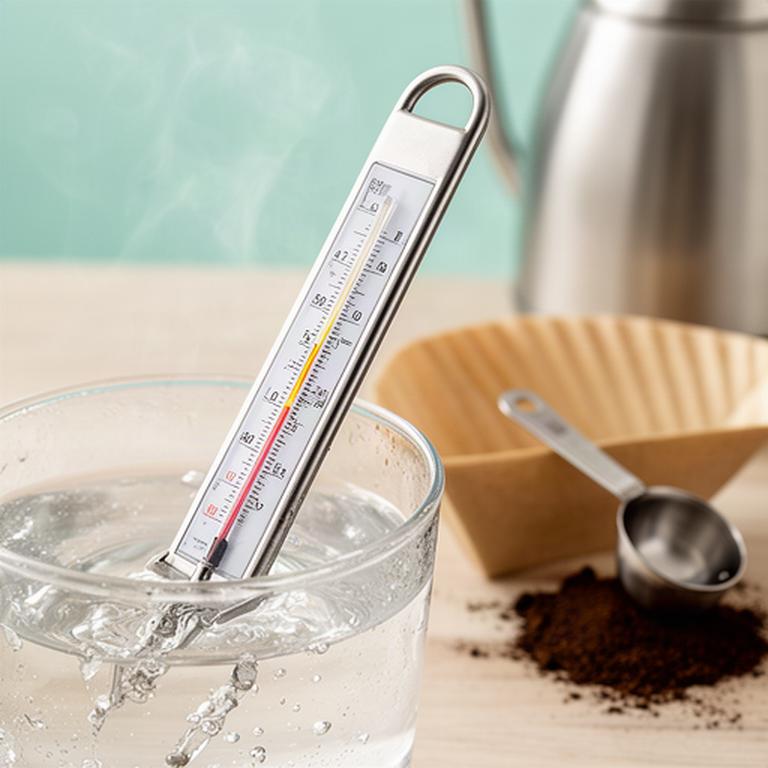 Thermometer in heissem Brühwasser neben Kaffeefilter und Messlöffel